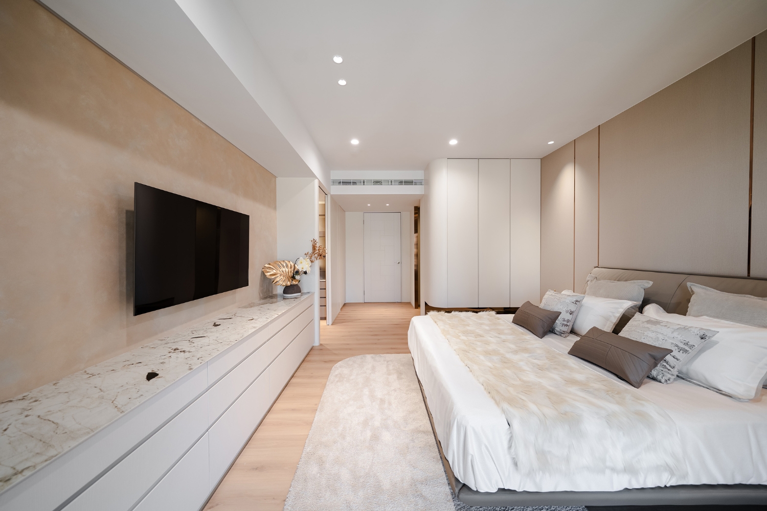 主臥室透過矽酸鈣板天花板平整化設計，將投射燈精準嵌入頂部，搭配大地色特殊漆電視牆與質感長櫃，展現簡約而不失層次的睡眠空間，平整的吊頂處理不僅隱藏管線，更讓室內高度在視覺上獲得延伸